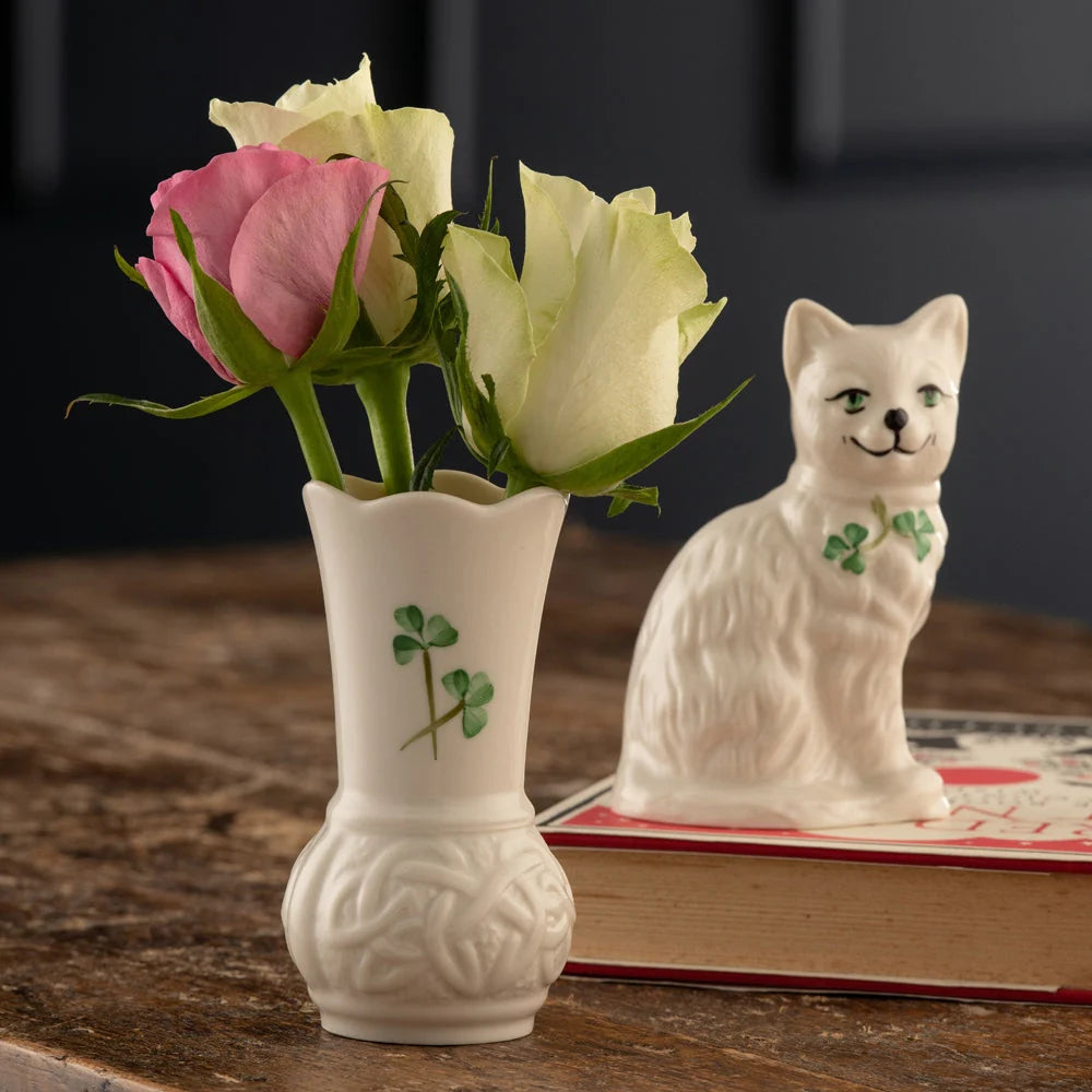 White vase with pink and white roses and a ceramic cat figurine on a wooden surface.
