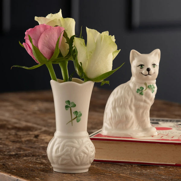 White vase with pink and white roses and a ceramic cat figurine on a wooden surface.