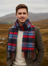 Man wearing a plaid scarf in a scenic outdoor setting with mountains.