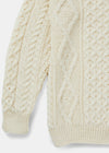 Close-up of a cream-colored knitted sweater with cable pattern on a light gray background