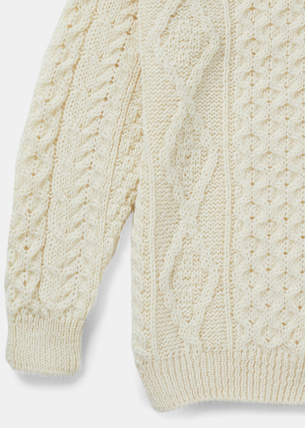 Close-up of a cream-colored knitted sweater with cable pattern on a light gray background