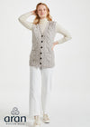Woman wearing a cable knit vest with buttons on a white background, branded 'Aran Woollen Mills'.