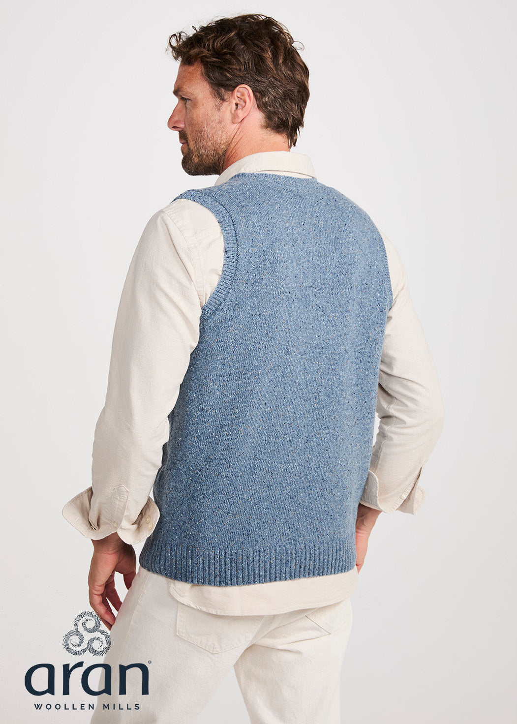 Man wearing a blue knitted vest over a white shirt on a white background, with 'Aran Woollen Mills' branding.