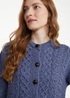 A woman with long wavy light brown hair wearing a textured blue cable-knit cardigan sweater with dark buttons, photographed against a clean white background.