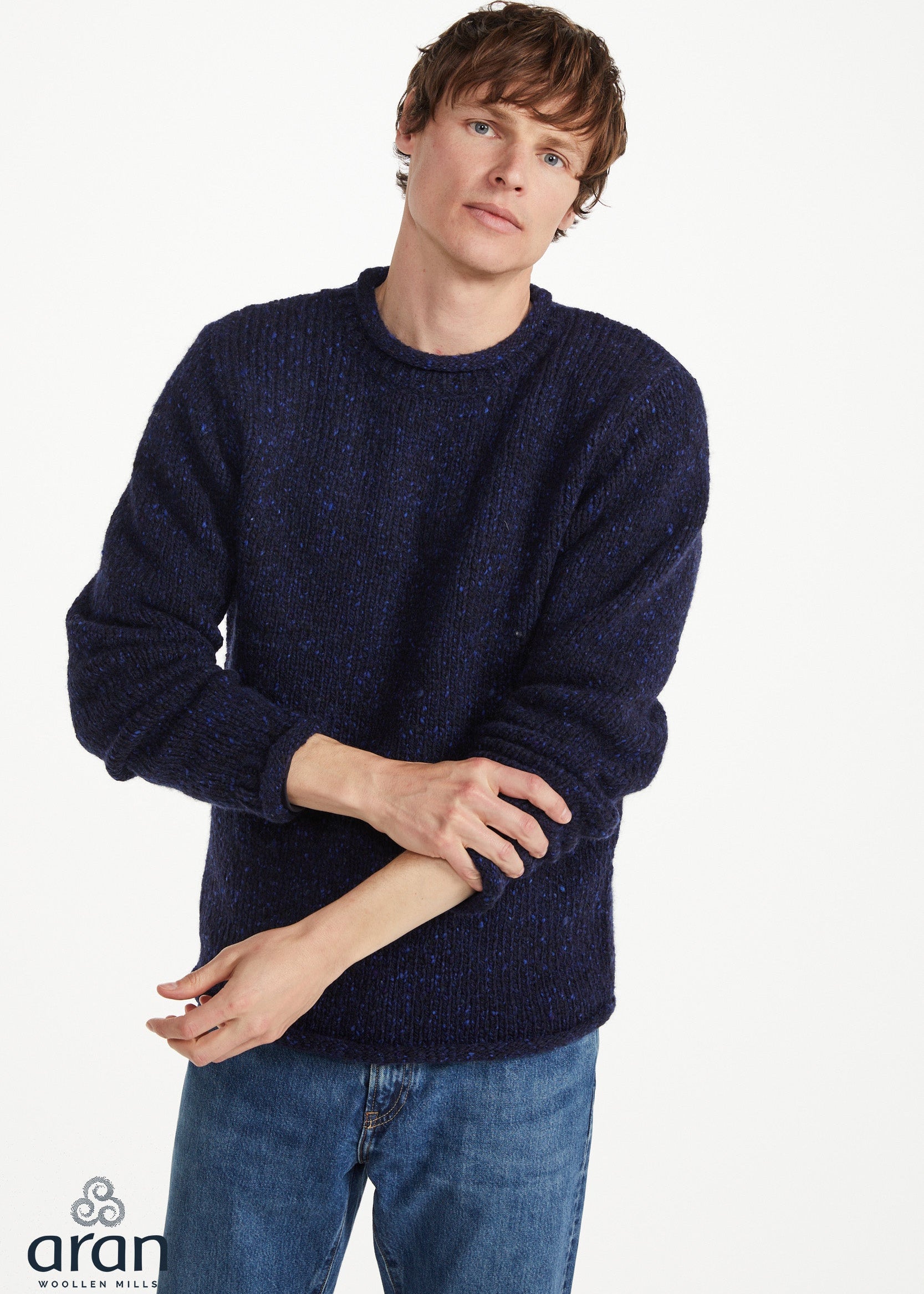 A man wearing a dark navy blue textured knit sweater and blue jeans, standing against a plain white studio background. The brand logo 'aran' is visible in the bottom-left corner.