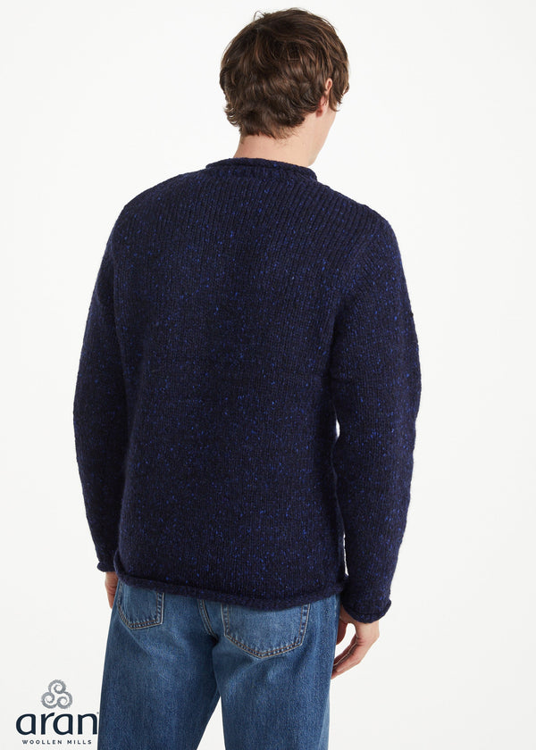 A man viewed from behind wearing a dark navy blue textured knit sweater and blue jeans against a plain white studio background.