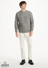 Man wearing a gray patterned sweater and white pants on a white background