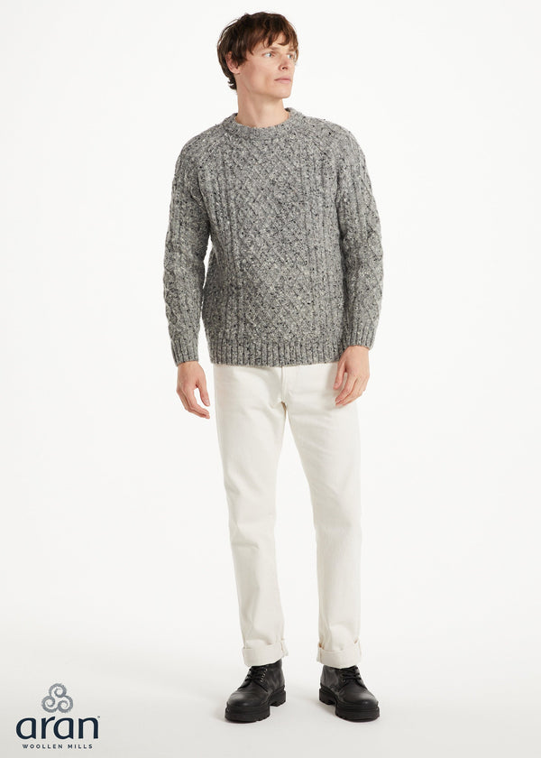 Man wearing a gray patterned sweater and white pants on a white background