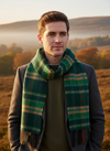 Man wearing a green plaid scarf with a scenic background of trees and mountains.