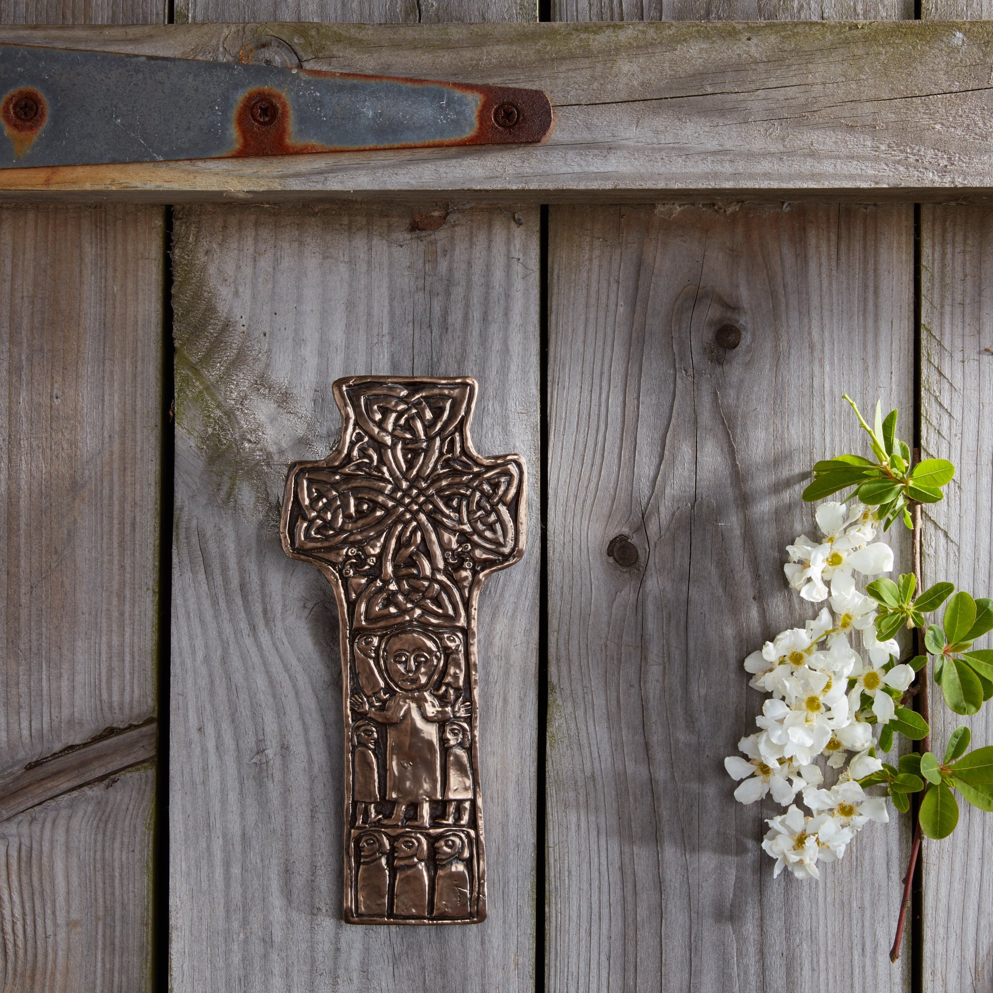 Bronze cross on a wooden surface with white flowers and green leaves