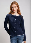 Woman wearing a navy blue cardigan over a white shirt with jeans on a light gray background