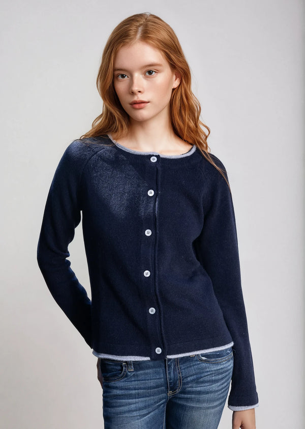 Woman wearing a navy blue cardigan over a white shirt with jeans on a light gray background