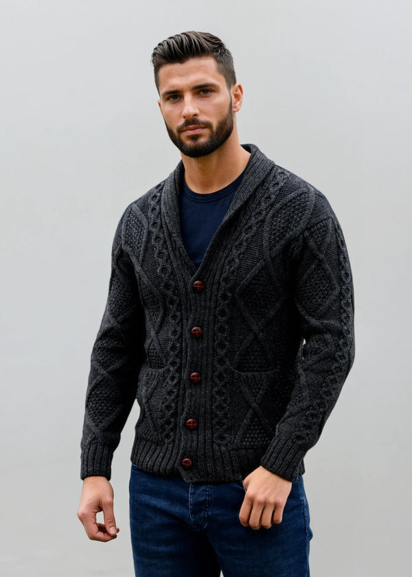 Man wearing a dark gray patterned aran cardigan over a blue shirt against a plain background
