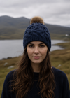 Woman wearing a blue knit beanie with a pom-pom in a scenic outdoor setting.