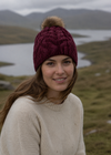 Woman wearing a maroon knit hat with a pom-pom in a mountainous landscape.