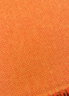 A close-up of an orange woven textile with a herringbone pattern and fringed edge, laid on a dark surface.