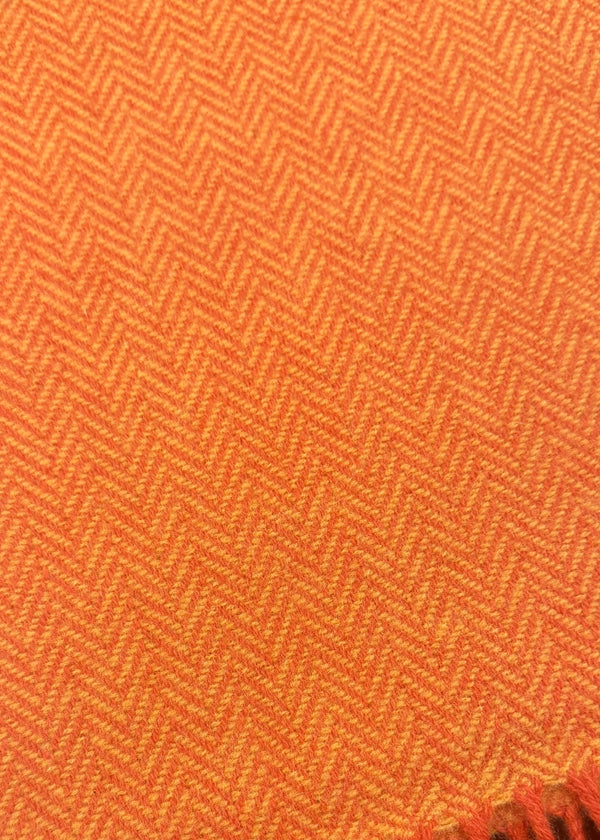 A close-up of an orange woven textile with a herringbone pattern and fringed edge, laid on a dark surface.