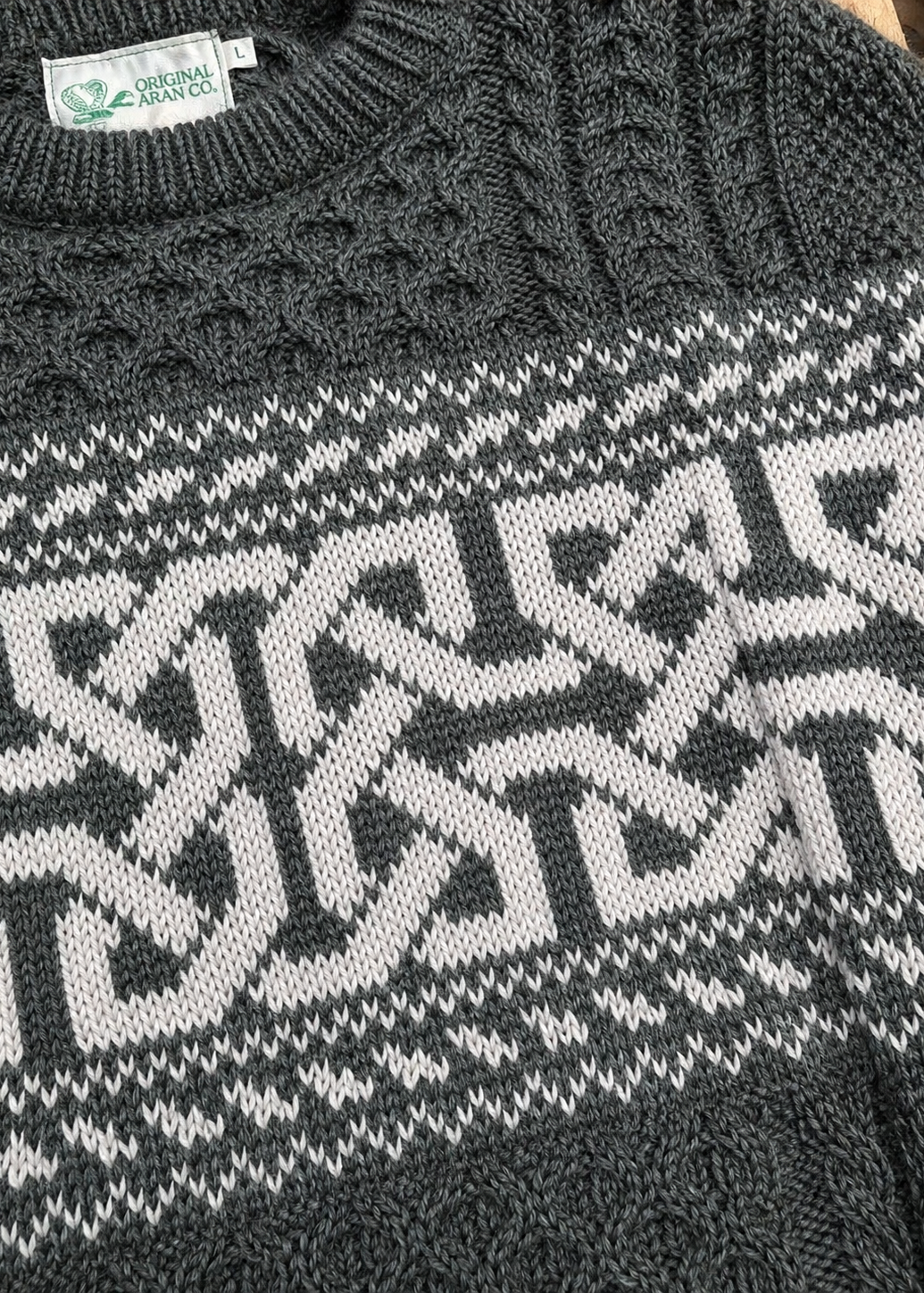 Close-up of a dark gray sweater with a geometric pattern, featuring a brand label.