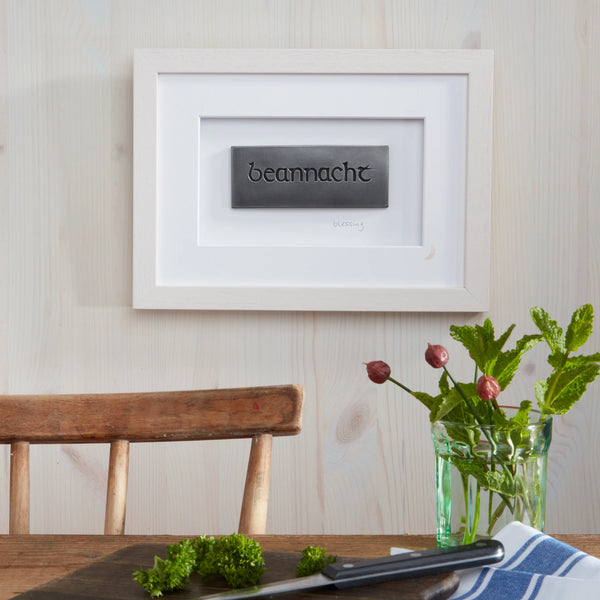 Framed artwork with the word 'beannacht' on a wall above a wooden chair and table.