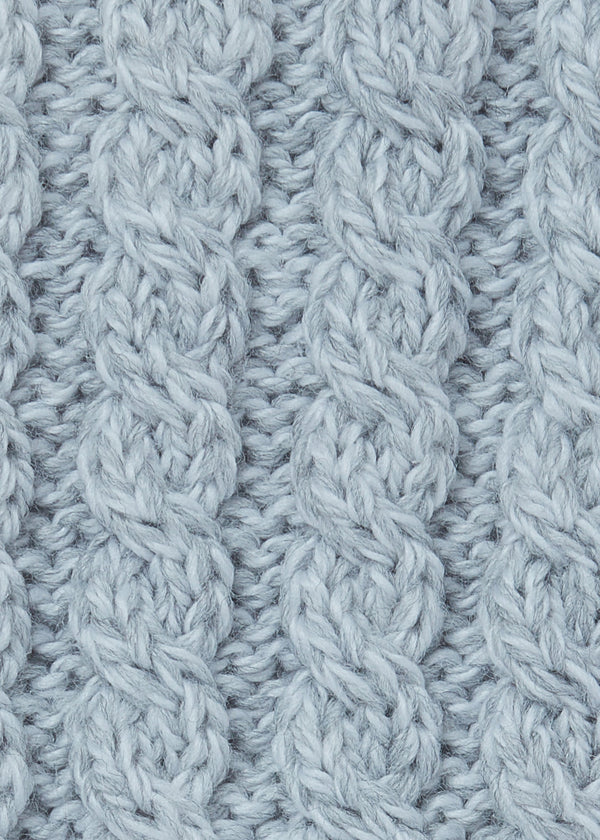 A close-up of a light blue-gray cable-knit fabric texture, showing the detailed knit pattern and soft yarn fibers.