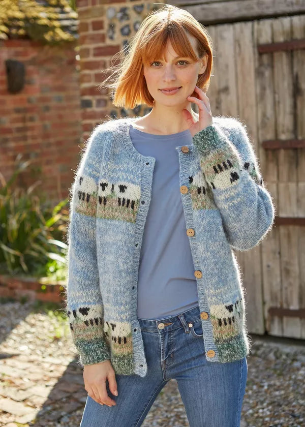 Woman wearing a patterned cardigan outdoors with a brick wall and wooden gate in the background.