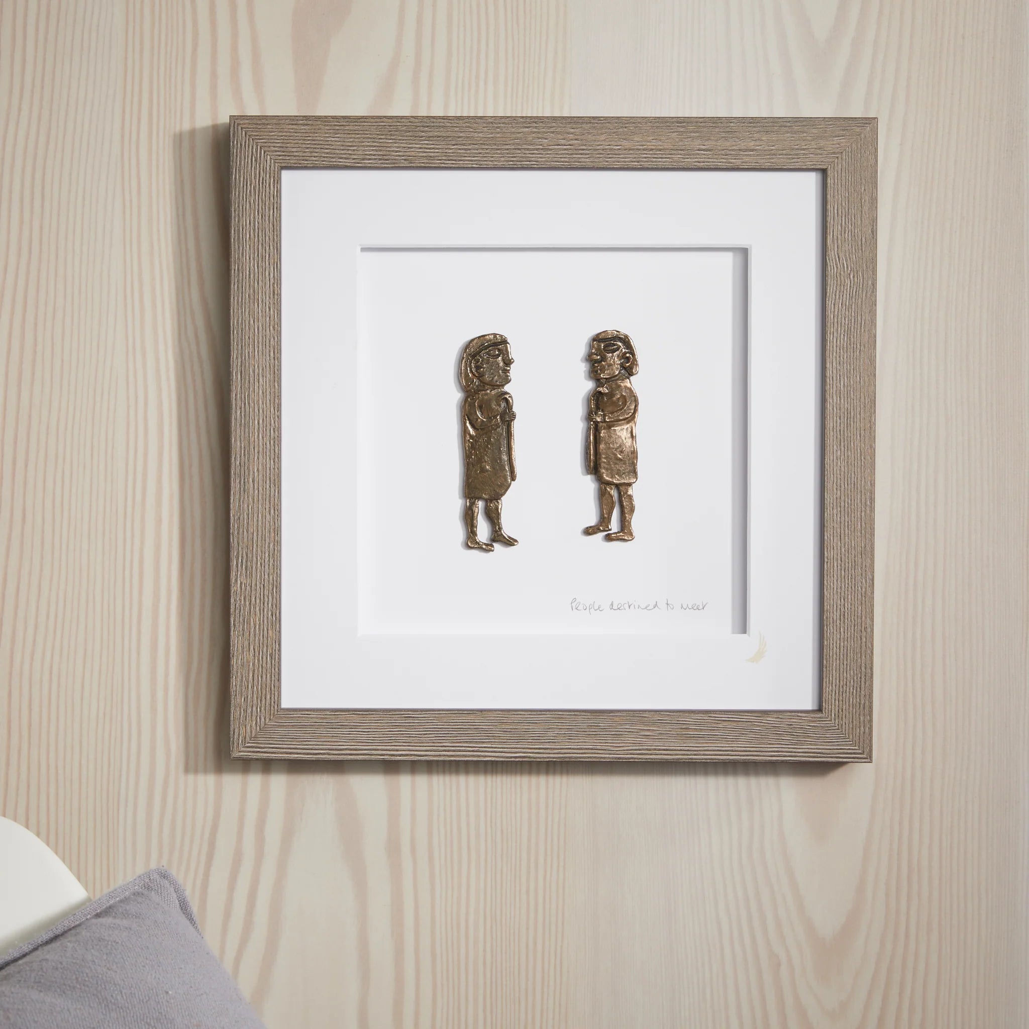 Framed artwork of two small figures on a wooden wall.
