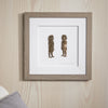 Framed artwork of two small figures on a wooden wall.