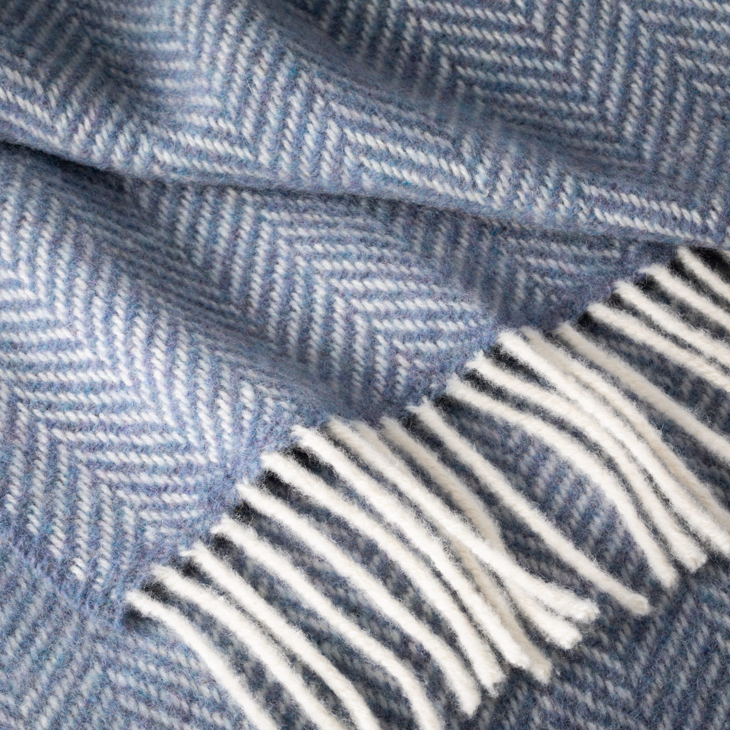 Close-up of a blue herringbone patterned fabric with white fringe.