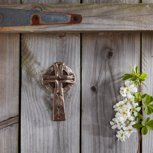 Decorative metal cross on a wooden wall with white flowers and green leaves.