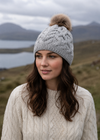 Woman wearing a cable knit beanie with a pom-pom in a scenic outdoor setting.