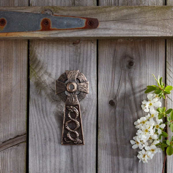Decorative metal cross on a wooden wall with white flowers and green leaves.