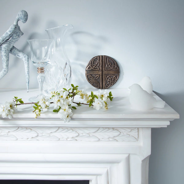 Decorative items on a white mantelpiece including a glass vase, sculpture, and floral branch.