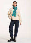 Person wearing a beige sweater, blue jeans, and a teal scarf on a white background
