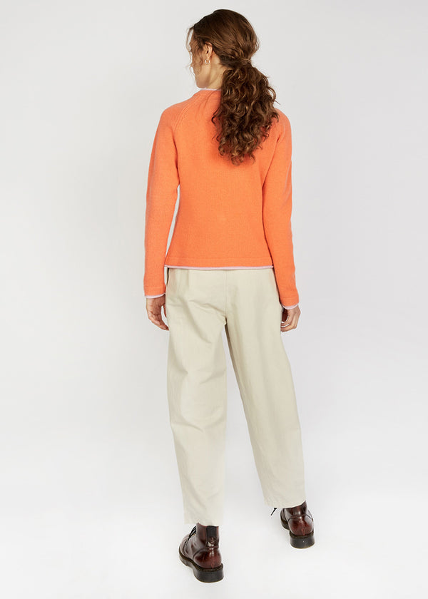 Person wearing an orange sweater and beige pants on a white background