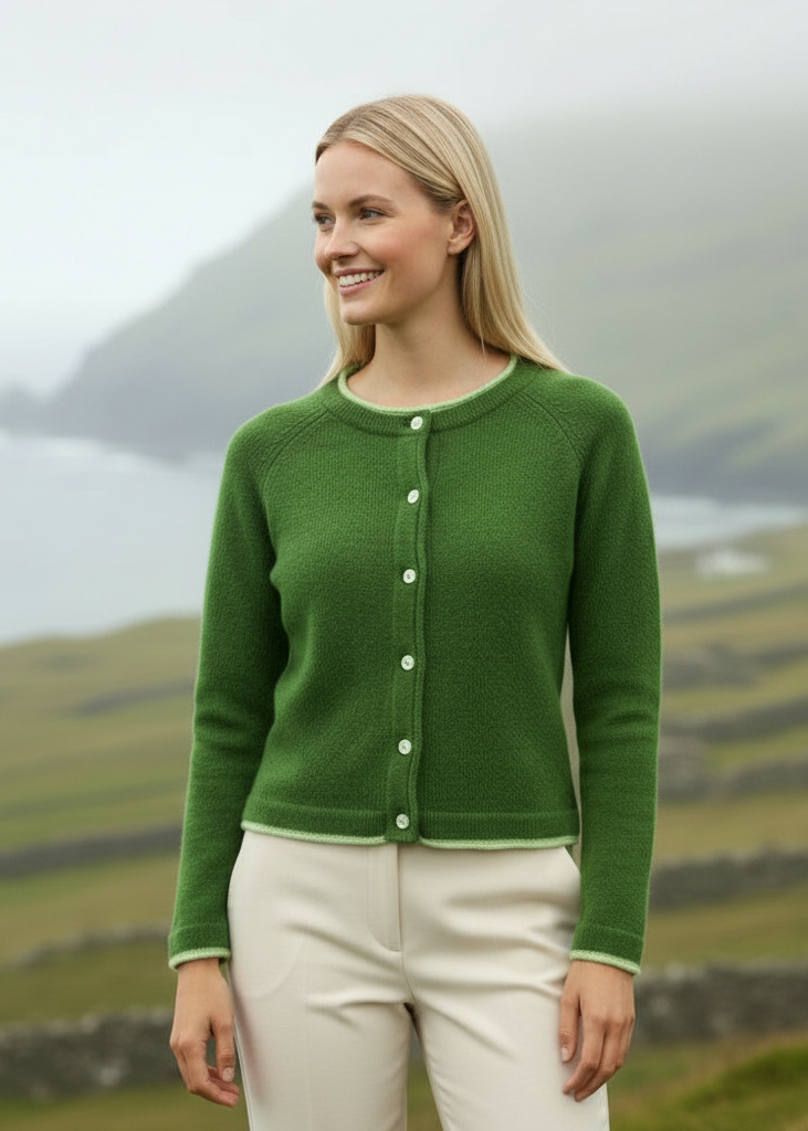 Woman wearing a green cardigan in a scenic outdoor setting with mountains and fields.