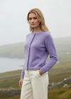 Woman wearing a purple cardigan standing in a scenic outdoor setting.