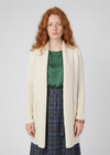 A model with red hair wearing a cream-colored, open-front, long-sleeve knit cardigan over a green satin top and a blue plaid skirt, standing against a light gray studio background.