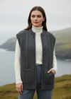 Woman wearing a gray knitted vest over a white turtleneck sweater with a scenic background.