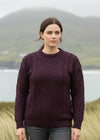 Woman wearing a purple sweater standing in a scenic outdoor setting with mountains and water.