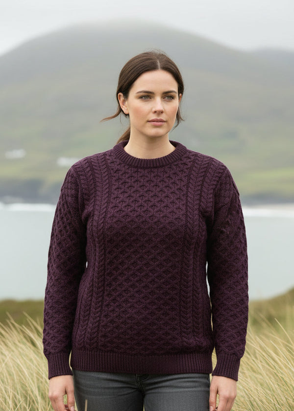 Woman wearing a purple sweater standing in a scenic outdoor setting with mountains and water.