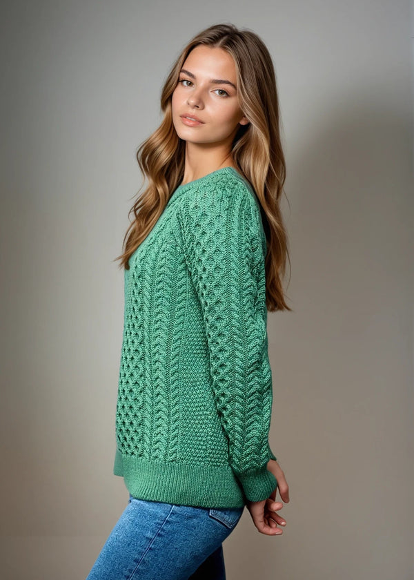 Woman wearing a green knitted aran sweater against a plain background