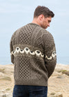 A man wearing a brown and cream cable-knit sweater with a sheep pattern, photographed from behind in an outdoor coastal setting. The brand name 'Arav Crafts' is visible in the bottom right corner.