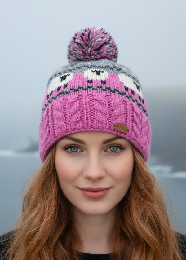 Person wearing a pink knitted beanie with a patterned design and pom-pom on a blurred natural background.