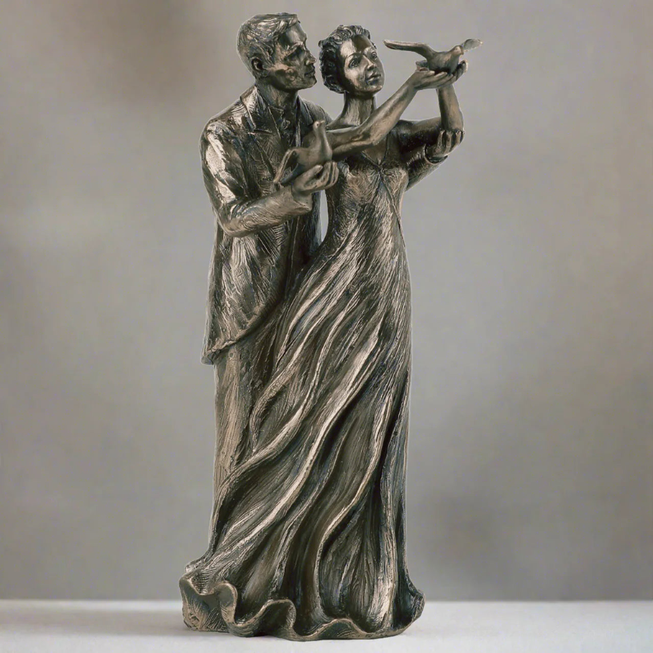 Bronze statue of a couple with a bird on a gray background