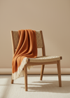 Wooden chair with a rust-colored blanket draped over it against a beige wall.