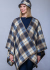 A woman modeling a plaid wrap poncho and matching bucket hat in navy, beige, and brown tones against a solid gray studio background.