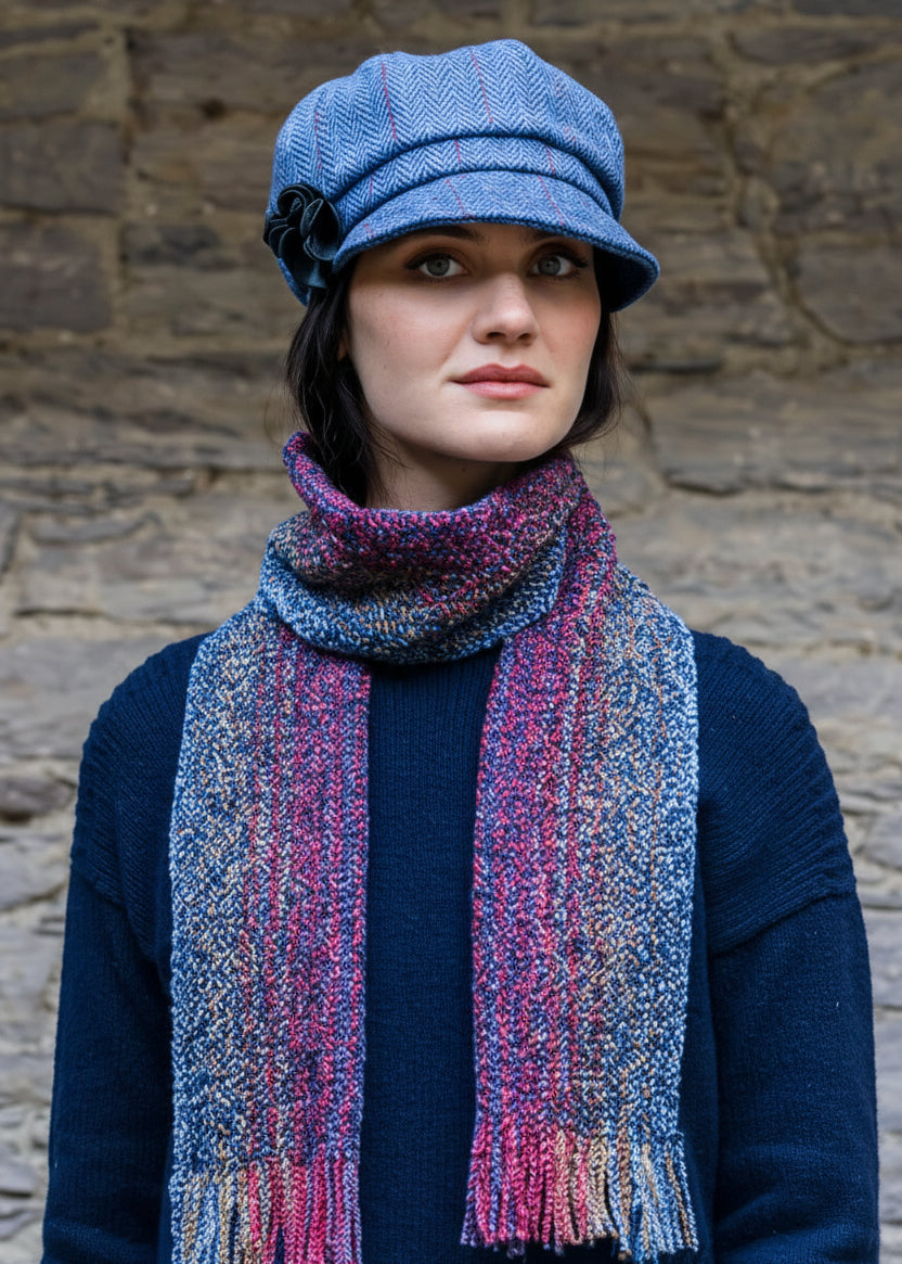 Person wearing a blue knit sweater, blue pants, and a colorful scarf against a stone wall.