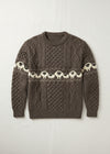 A brown cable-knit crewneck sweater featuring a horizontal band of cream-colored sheep with black faces across the chest and upper sleeves, laid flat on a light off-white background.
