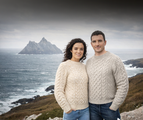 Two people wearing cable knit sweaters standing on a coastal landscape with Skellig Michael in the background.