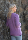 Woman wearing a purple sweater standing against a stone wall